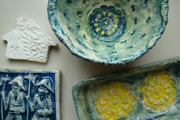 zdjęcie wytworów ceramicznych, wykonanych przez uczestników warszatów. Miska, kafel, kwadratowy talerz, w odcieniach żółtych i niebieskich.